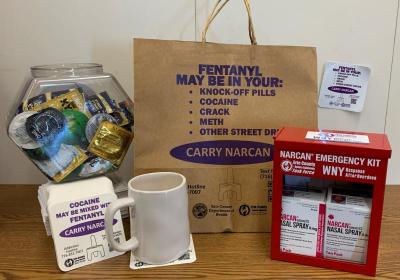 Grouping of materials with harm reduction messages - brown paper bags, condoms, Narcan boxes, drink coasters, magnets